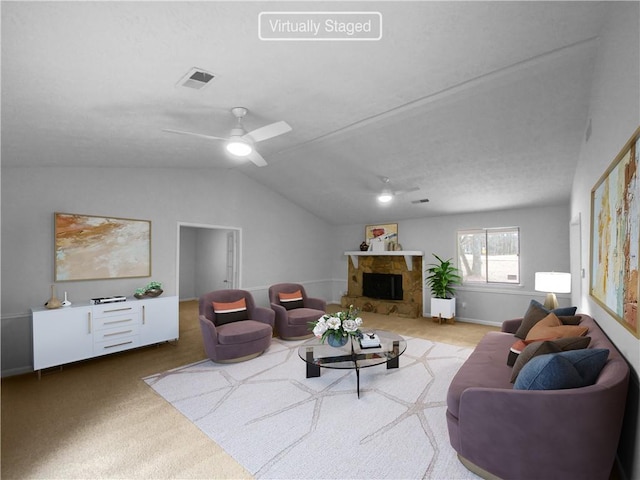 carpeted living room with ceiling fan, vaulted ceiling, and a stone fireplace