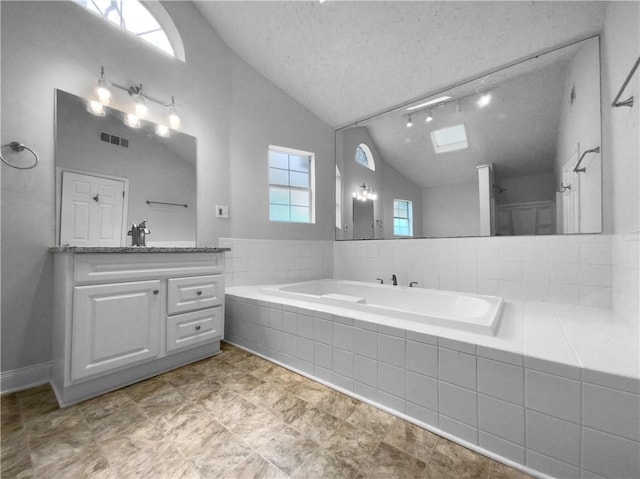 bathroom featuring vanity, a textured ceiling, a relaxing tiled tub, and vaulted ceiling