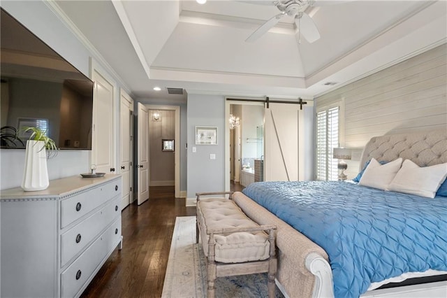 bedroom with a barn door, visible vents, a raised ceiling, dark wood-style floors, and ornamental molding