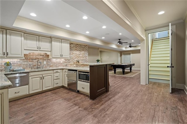 kitchen featuring crown molding, a warming drawer, stainless steel microwave, wood finished floors, and a peninsula