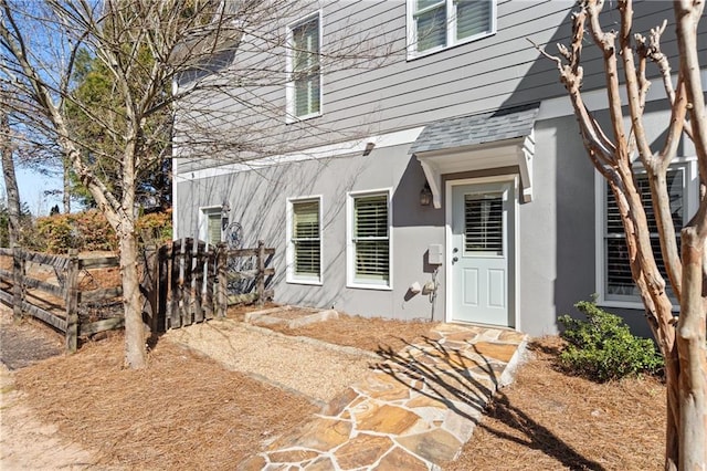 view of exterior entry with roof with shingles, fence, and stucco siding