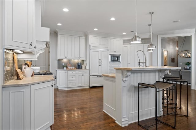 kitchen featuring a breakfast bar area, dark wood-type flooring, built in appliances, light countertops, and white cabinetry