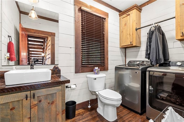 bathroom with toilet, vanity, washer and dryer, wood walls, and wood-type flooring