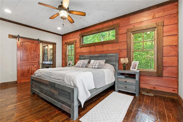 bedroom featuring wooden walls, crown molding, a barn door, dark hardwood / wood-style flooring, and ceiling fan