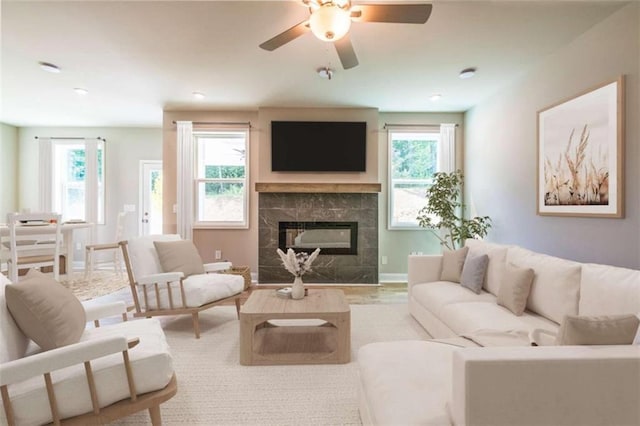 living room with ceiling fan, light wood-type flooring, a premium fireplace, and a wealth of natural light