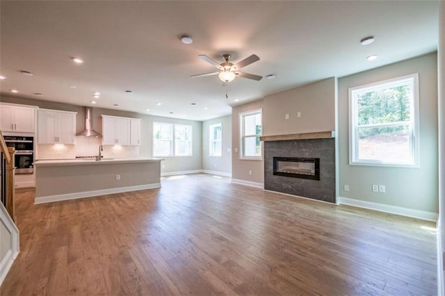 unfurnished living room with a tiled fireplace, ceiling fan, sink, and light wood-type flooring