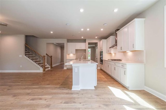 kitchen with sink, light hardwood / wood-style floors, white cabinetry, stainless steel gas stovetop, and an island with sink