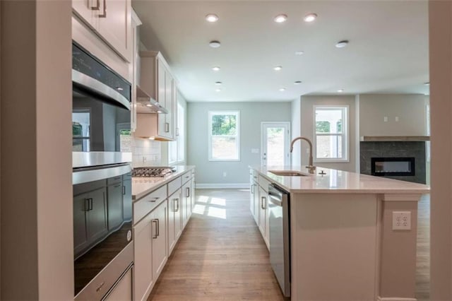 kitchen with sink, stainless steel appliances, an island with sink, decorative backsplash, and a fireplace