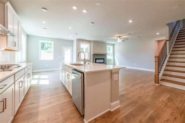 kitchen featuring appliances with stainless steel finishes, light wood-type flooring, sink, a center island with sink, and white cabinetry