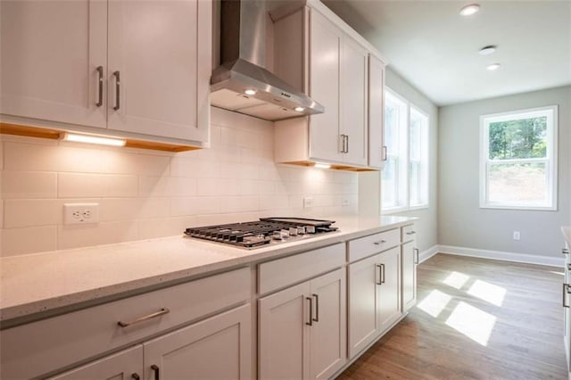 kitchen featuring white cabinets, light stone countertops, stainless steel gas stovetop, and wall chimney exhaust hood