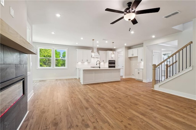 4002 Adler Cir, Buford, GA 30519 - unfurnished living room with a ceiling fan, light wood-style floors, a tiled fireplace, baseboards, and visible vents