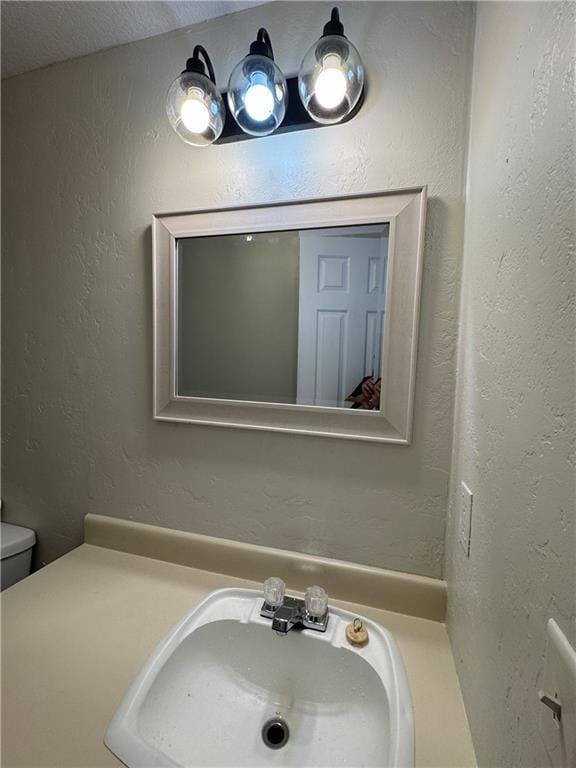 bathroom with a textured wall, a sink, and toilet