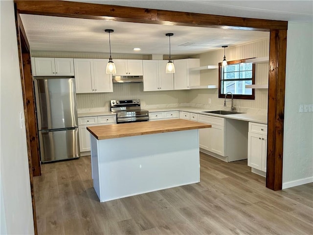 kitchen with under cabinet range hood, stainless steel appliances, a sink, white cabinetry, and hanging light fixtures