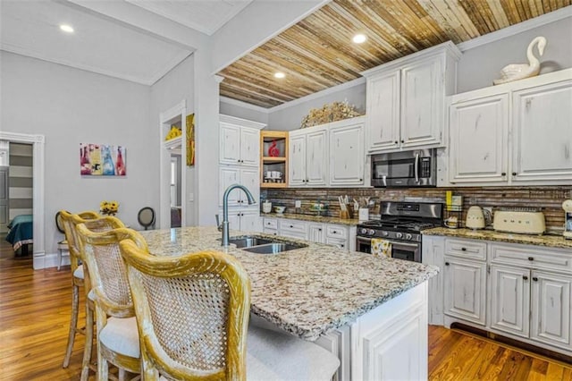 kitchen featuring decorative backsplash, appliances with stainless steel finishes, a kitchen island with sink, sink, and white cabinets