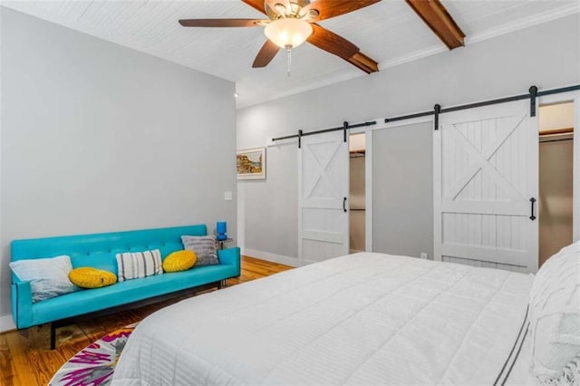 bedroom featuring a barn door, ceiling fan, beamed ceiling, and wood-type flooring