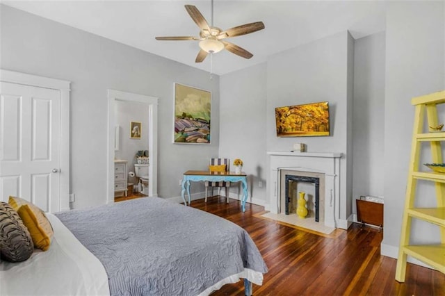 bedroom featuring ceiling fan, dark hardwood / wood-style flooring, a fireplace, and connected bathroom