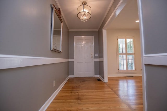 entryway featuring visible vents, wood finished floors, an inviting chandelier, crown molding, and baseboards