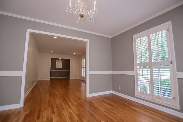 spare room featuring a chandelier, baseboards, wood finished floors, and crown molding