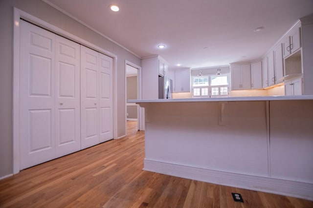 kitchen featuring light wood finished floors, stainless steel fridge, white cabinets, and a peninsula