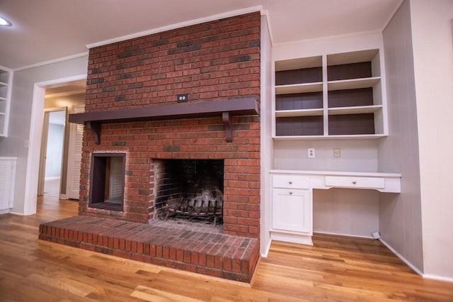 unfurnished living room featuring a brick fireplace, crown molding, baseboards, light wood-type flooring, and built in study area