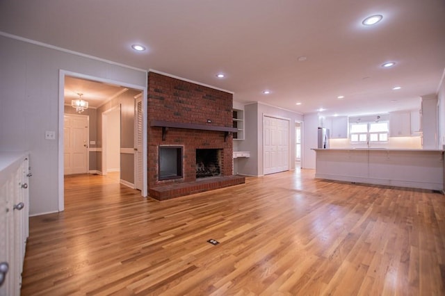 unfurnished living room with a sink, a fireplace, light wood-type flooring, and ornamental molding