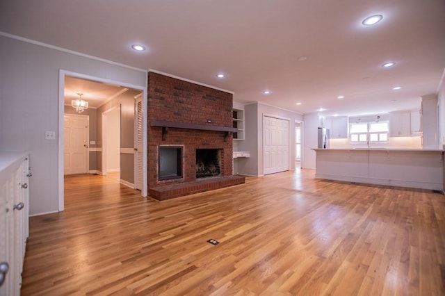 unfurnished living room with a fireplace, light wood-type flooring, crown molding, and a sink