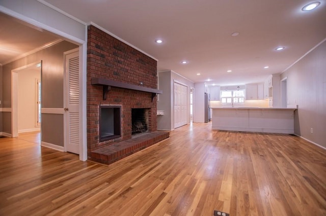 unfurnished living room featuring baseboards, recessed lighting, a fireplace, light wood-style floors, and crown molding