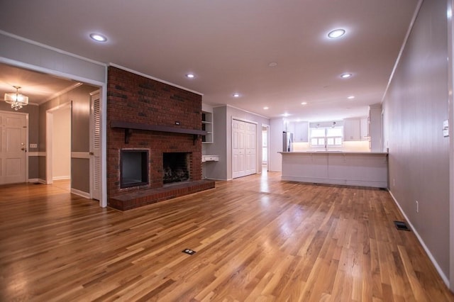 unfurnished living room featuring light wood finished floors, visible vents, a brick fireplace, and crown molding