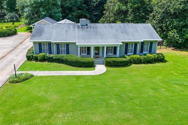 cape cod-style house featuring driveway, covered porch, a front yard, brick siding, and a chimney