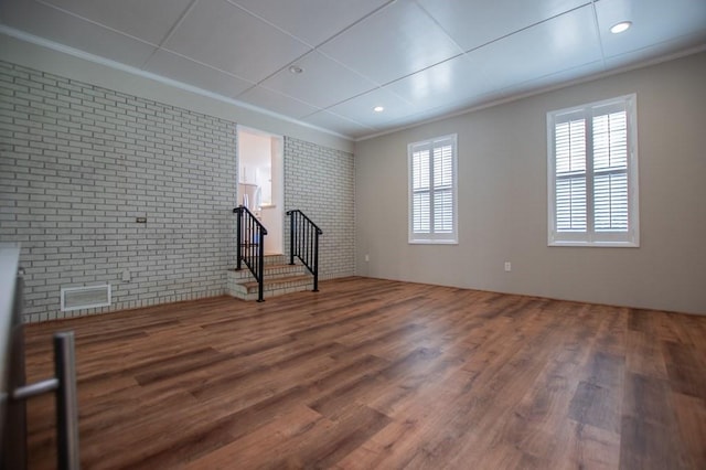 unfurnished room featuring wood finished floors, brick wall, and ornamental molding