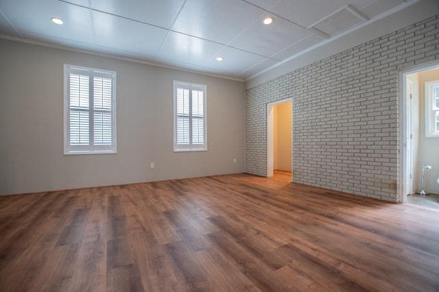 unfurnished room with recessed lighting, wood finished floors, brick wall, and ornamental molding