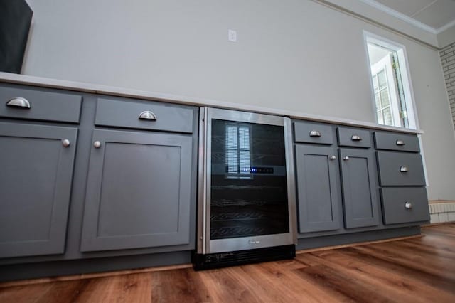 bar featuring wood finished floors, beverage cooler, and ornamental molding