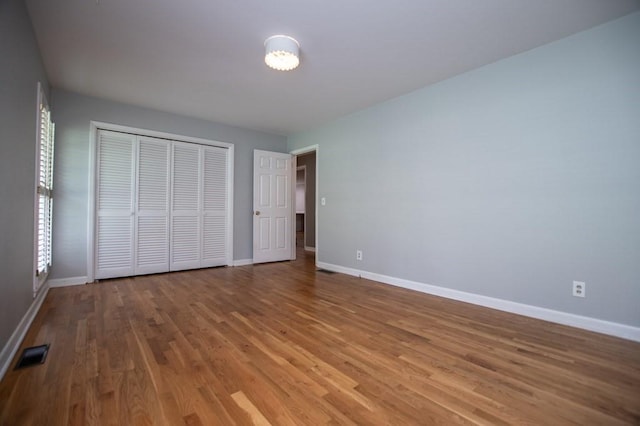 unfurnished bedroom featuring a closet, baseboards, visible vents, and wood finished floors