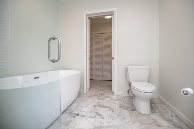 bathroom featuring a closet, baseboards, toilet, and a soaking tub