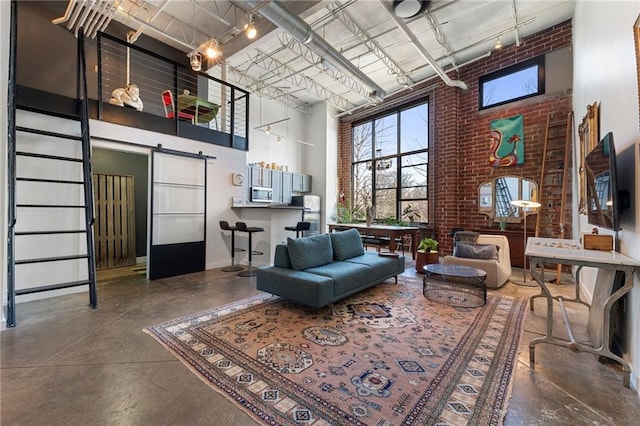 living room featuring concrete flooring, brick wall, a barn door, and a towering ceiling