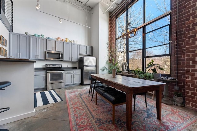 kitchen featuring brick wall, appliances with stainless steel finishes, a towering ceiling, and gray cabinetry