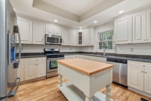 kitchen featuring light hardwood / wood-style floors, sink, white cabinets, stainless steel appliances, and a tray ceiling