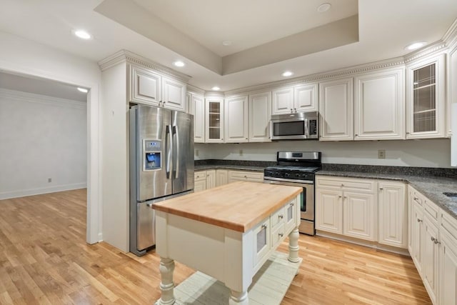 kitchen with butcher block countertops, appliances with stainless steel finishes, white cabinetry, light hardwood / wood-style flooring, and a tray ceiling