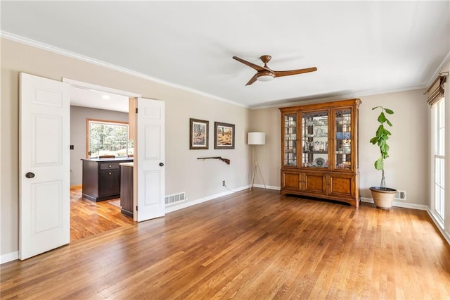 unfurnished room with baseboards, visible vents, crown molding, and light wood finished floors