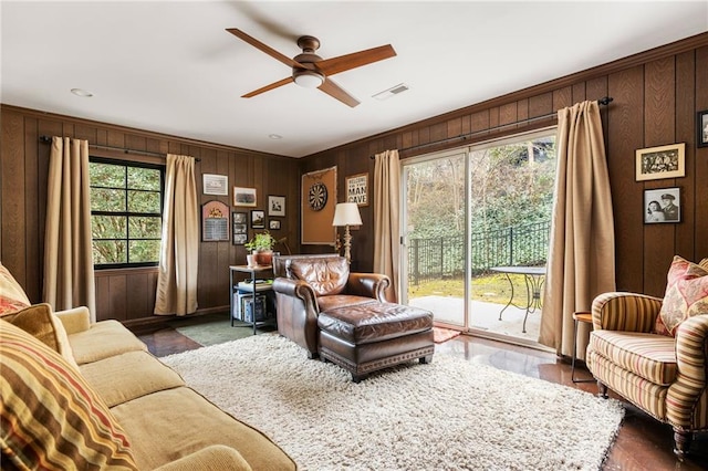 living room with wood walls, ceiling fan, and visible vents