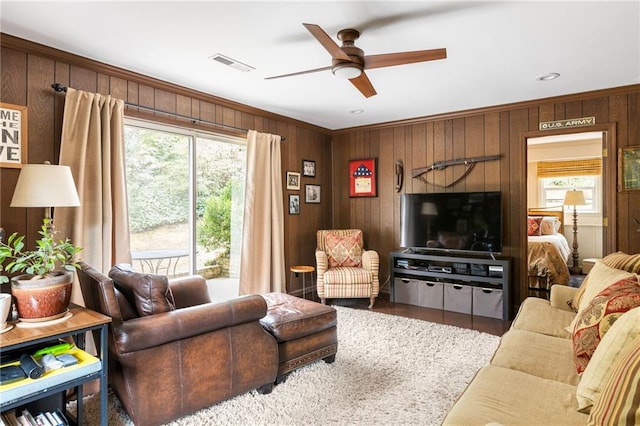 living room with a ceiling fan, visible vents, ornamental molding, and wooden walls