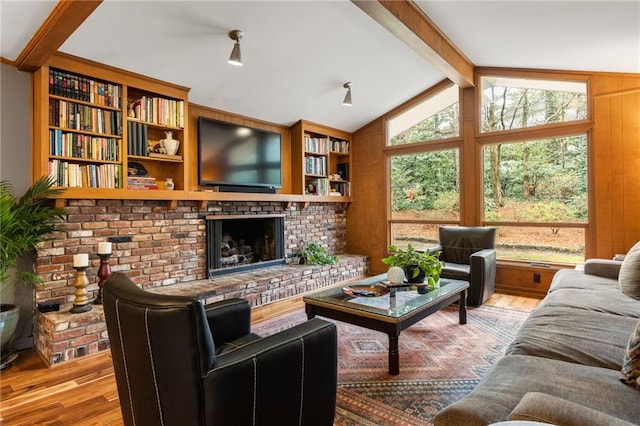 living area featuring lofted ceiling with beams, a brick fireplace, and wood finished floors