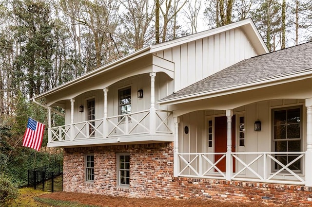 view of front facade featuring board and batten siding, covered porch, roof with shingles, and brick siding