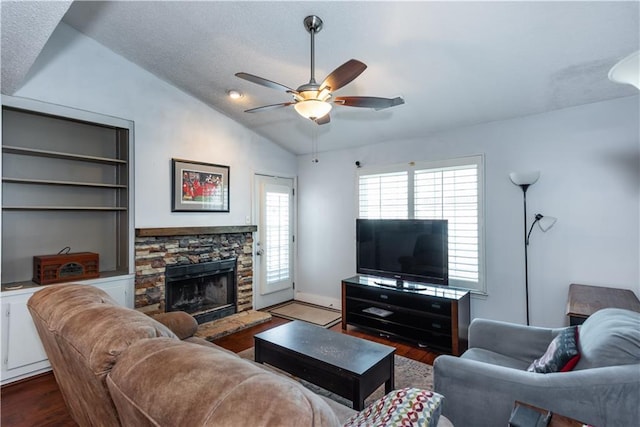 living room featuring dark wood-style floors, a stone fireplace, ceiling fan, and vaulted ceiling