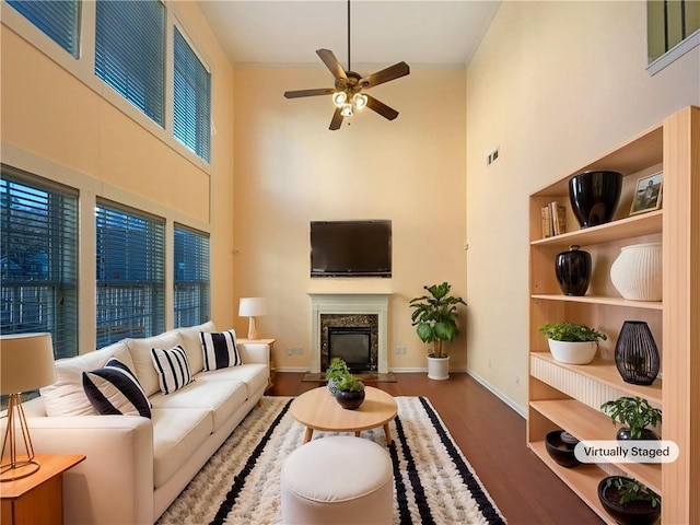 living room with hardwood / wood-style floors, a premium fireplace, ceiling fan, and a high ceiling