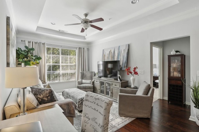 living room featuring dark wood-type flooring, ceiling fan, crown molding, and a tray ceiling