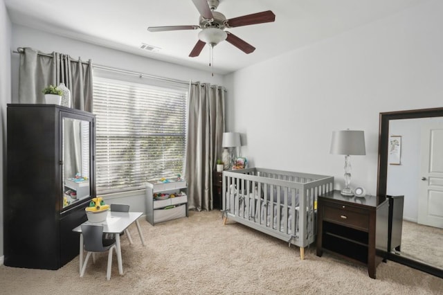 carpeted bedroom with a crib and ceiling fan