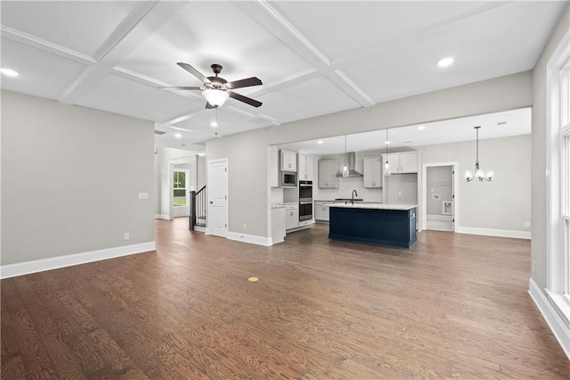 unfurnished living room with dark wood-type flooring, a sink, coffered ceiling, baseboards, and ceiling fan with notable chandelier