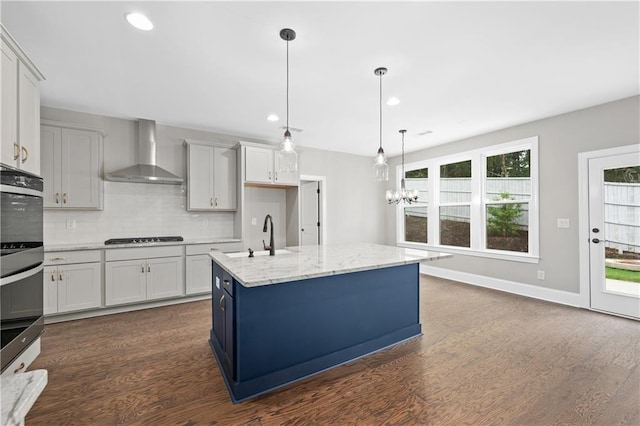 kitchen with a sink, dark wood finished floors, wall chimney range hood, backsplash, and cooktop