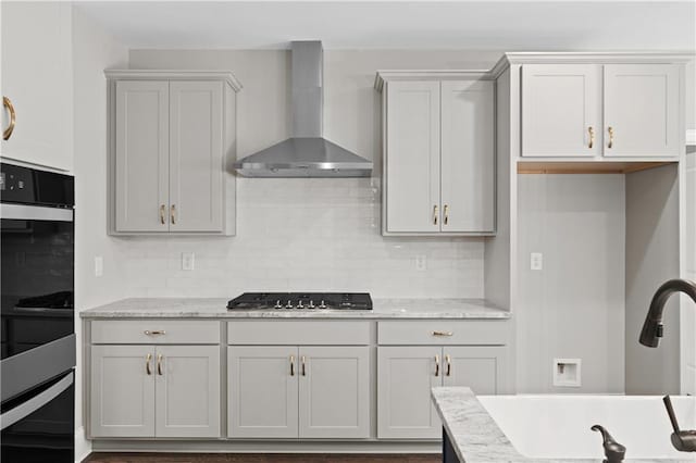 kitchen featuring double oven, a sink, gas stovetop, backsplash, and wall chimney exhaust hood